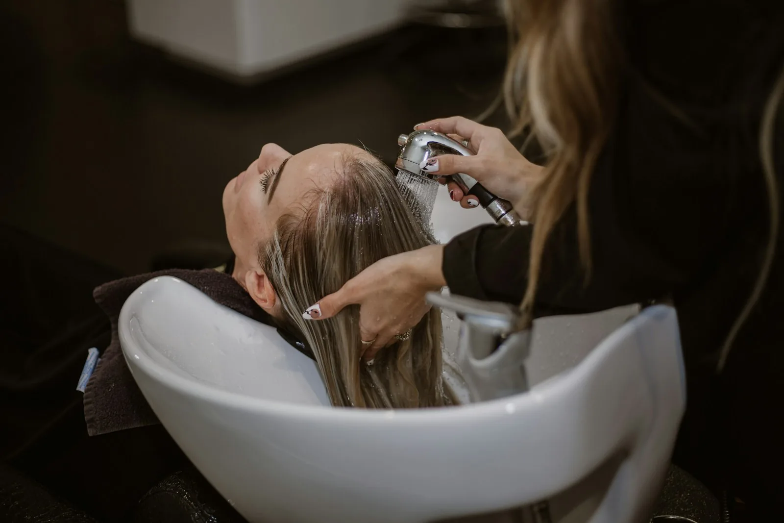 Client reclined at the wash basin while Dana rinses her hair in the dark-toned studio